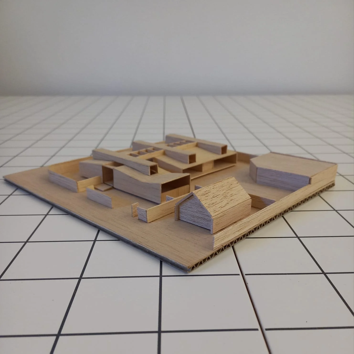 Maqueta de un desarrollo urbano con estructuras de madera en una base de cartón, sobre una superficie de azulejos blancos con líneas negras.