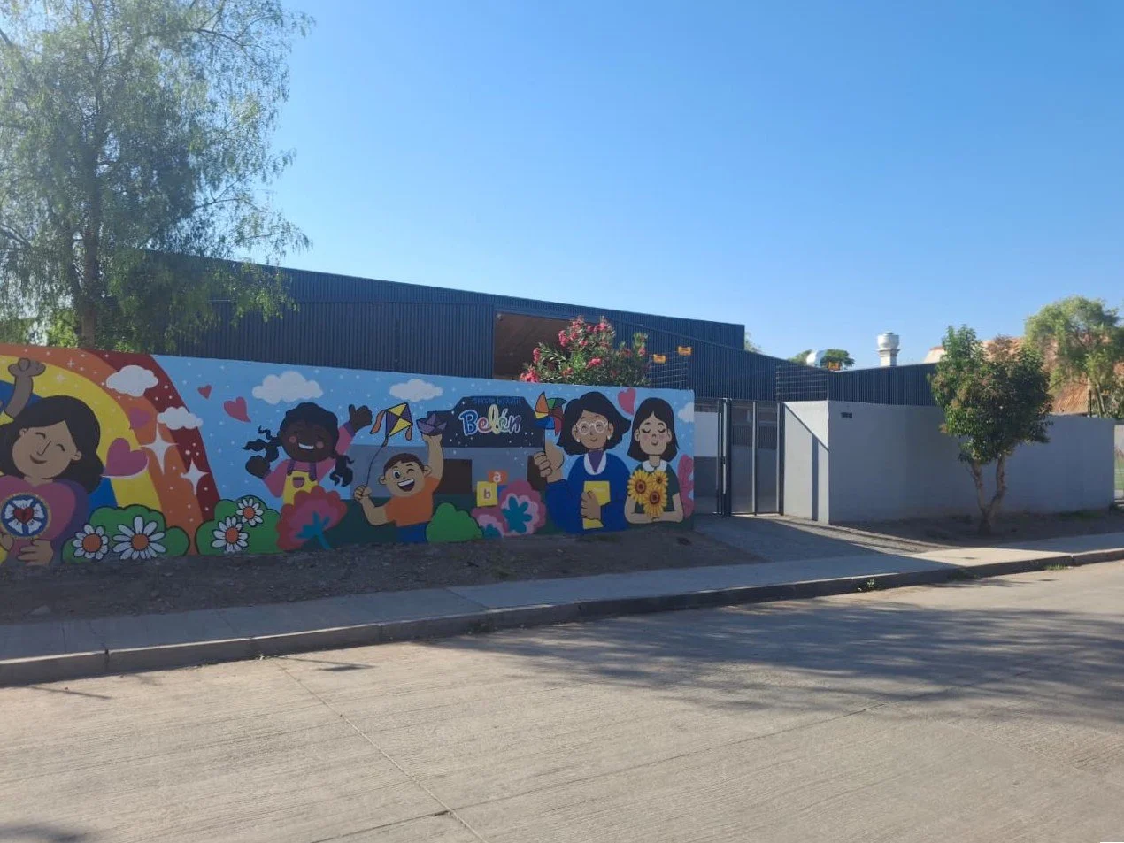 Mural colorido en la pared de un espacio infantil con dibujos de niños, flores y temáticas alegres.