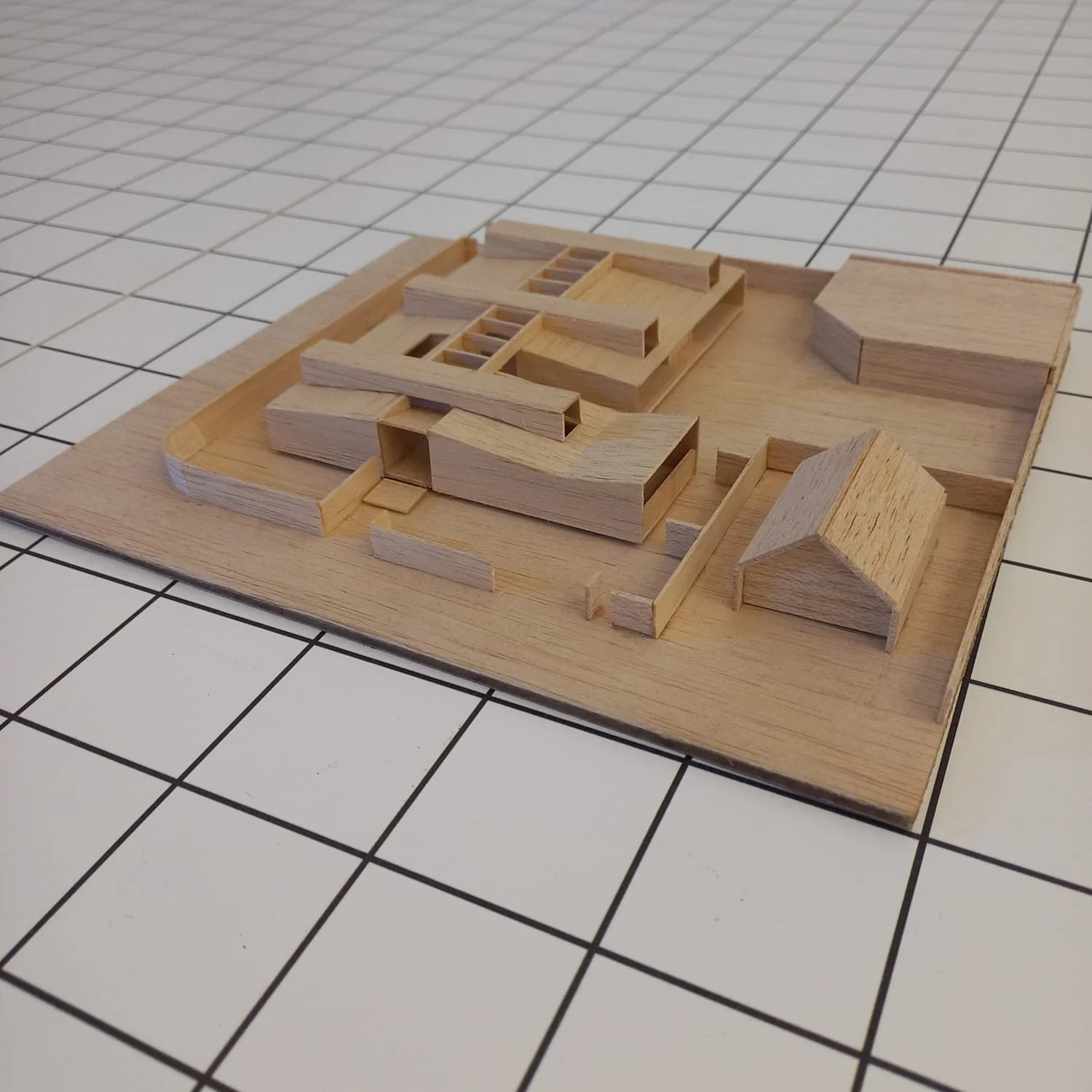 Maqueta de un edificio en construcción hecha de madera sobre una base de madera y una superficie de baldosas blancas con bordes negros.