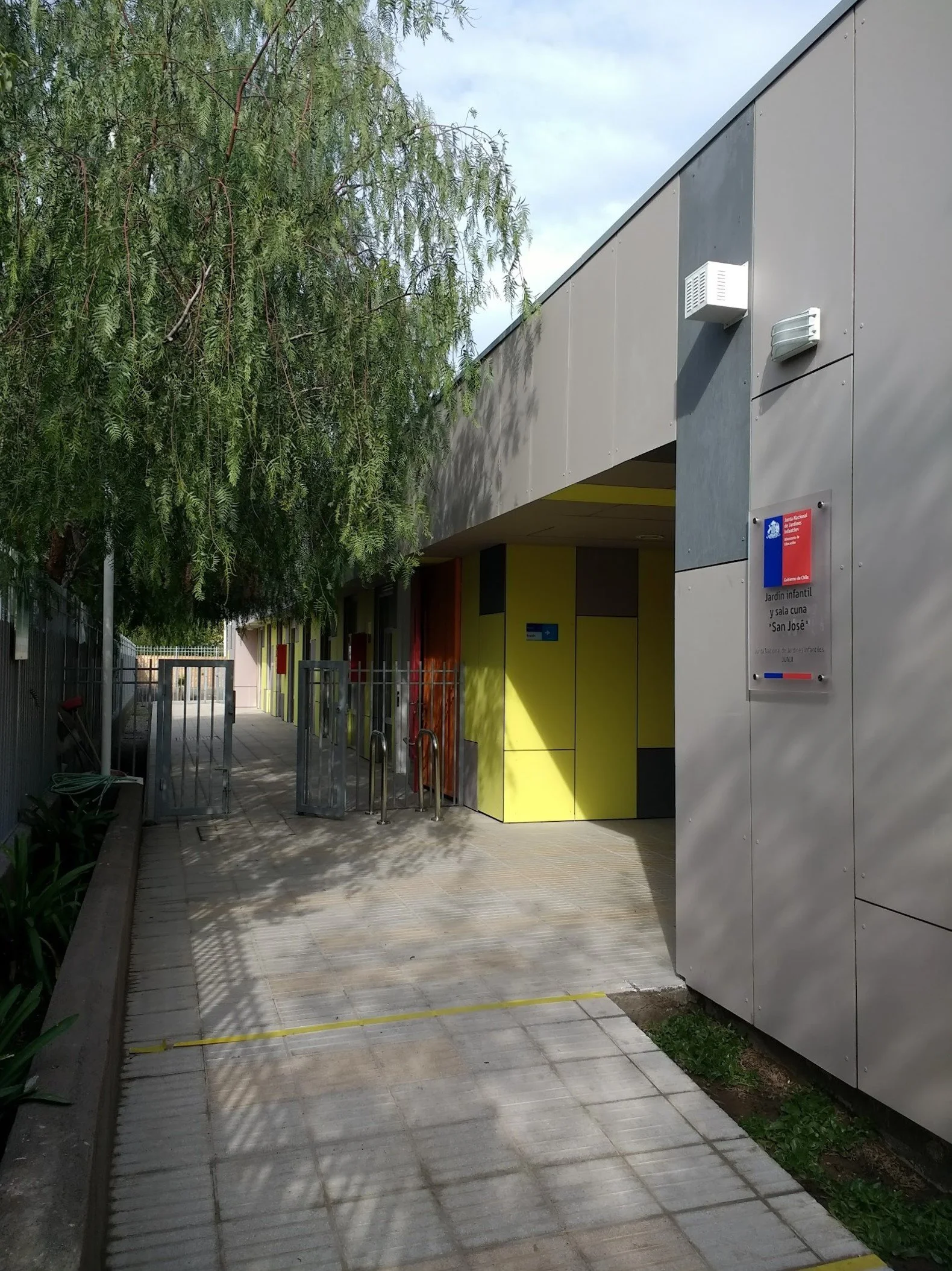 Entrada a un jardín infantil con señalización en español y una estructura moderna cerca de un árbol de gran tamaño.