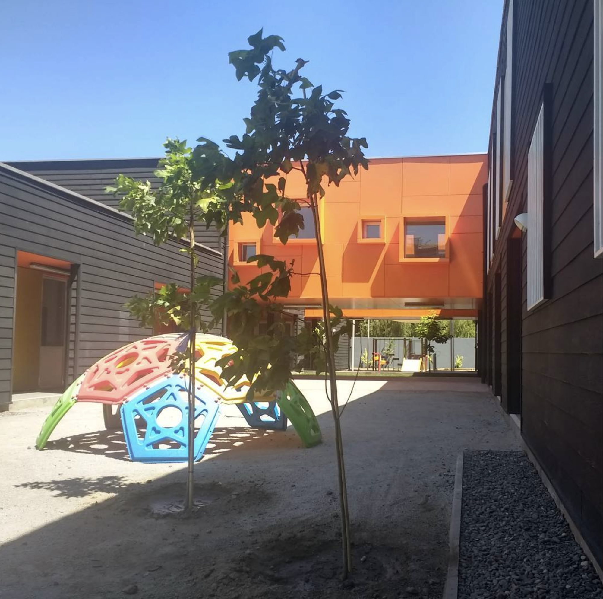Área peatonal con área de juegos y árboles, rodeada de edificios de diseño moderno.