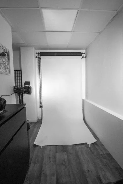 Photography backdrop stand with a white paper roll in a room with wood flooring and white walls.