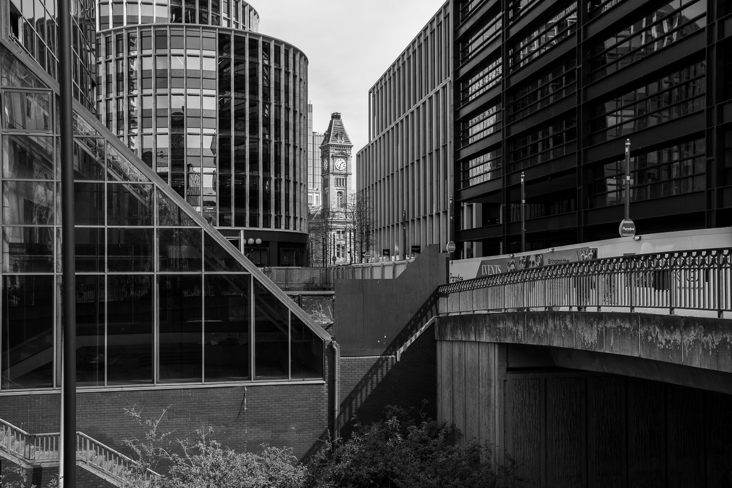 Black and white photo of Birmingham Museum & Art Gallery’s tower framed between modern buildings, taken from the pedestrian bridge near the Library of Birmingham.