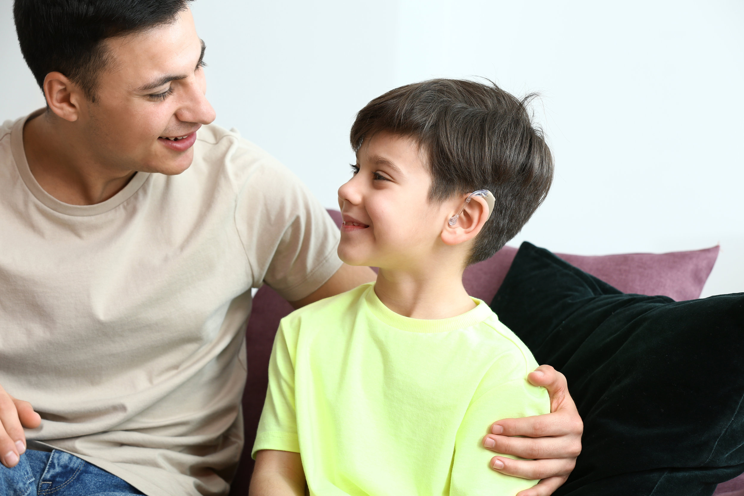 Young man and his son with hearing aid at home