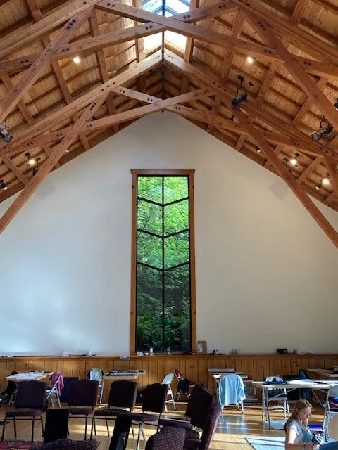 Light-filled cathedral studio space on Whidbey Island with tall timber beams and a tree-framed window — where a rewilding journey unfolded through art and creative expression