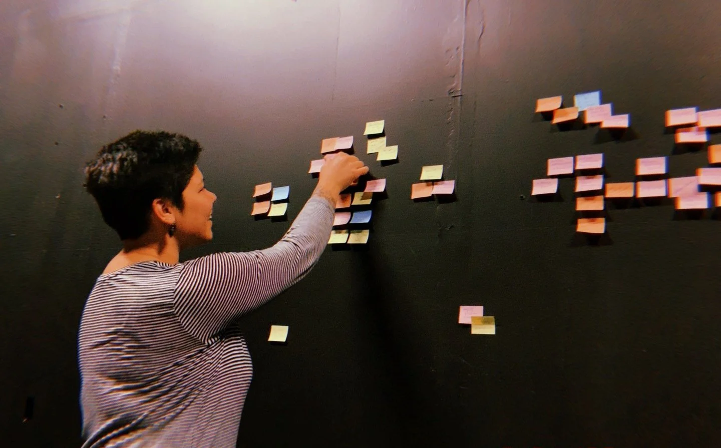 Pauline smiling, arranging colorful post-its with writing on them on a black wall