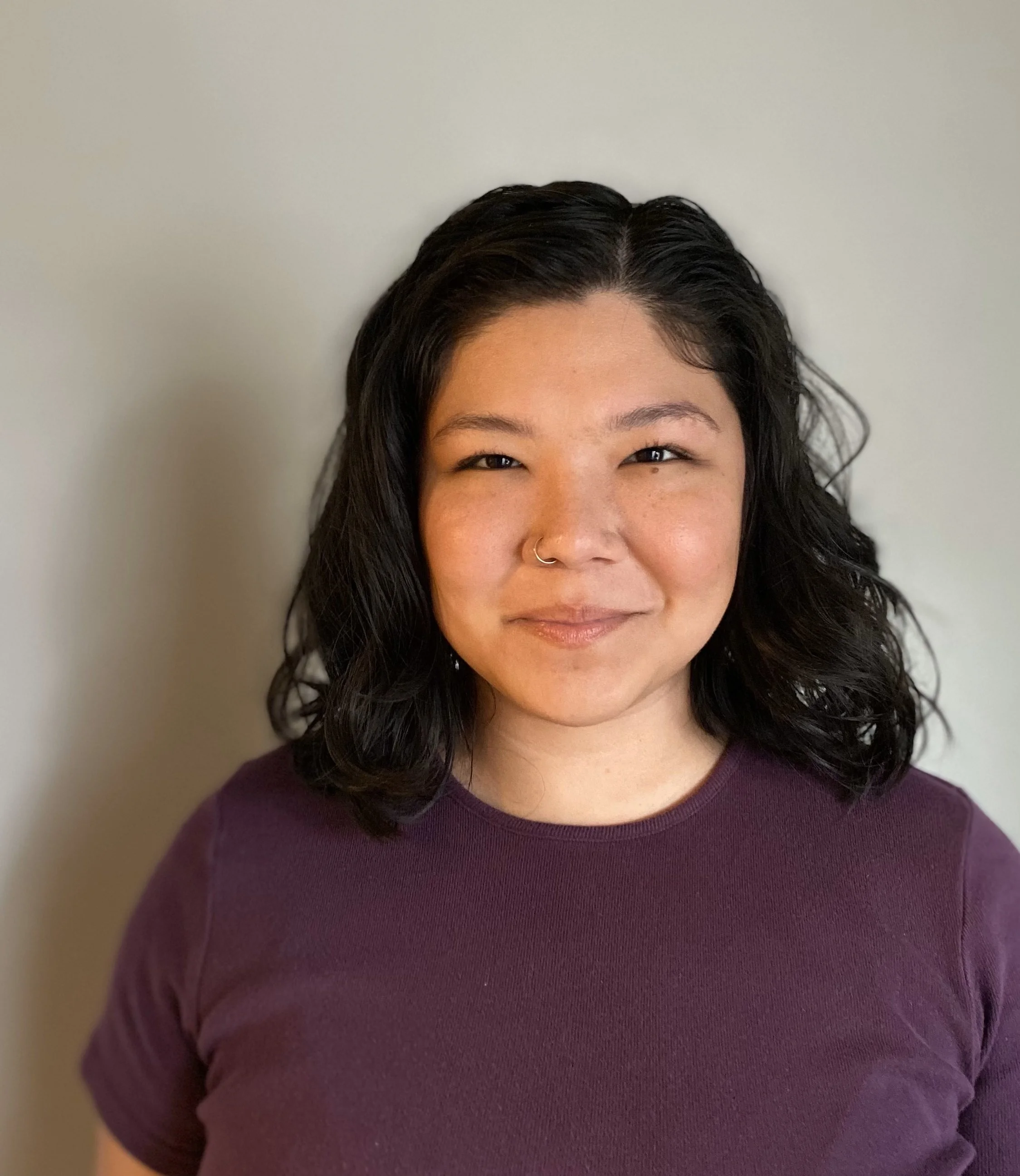 Pauline, with black wavy shoulder-length hair, light tan skin, a nose ring, and a twinkle in her eye