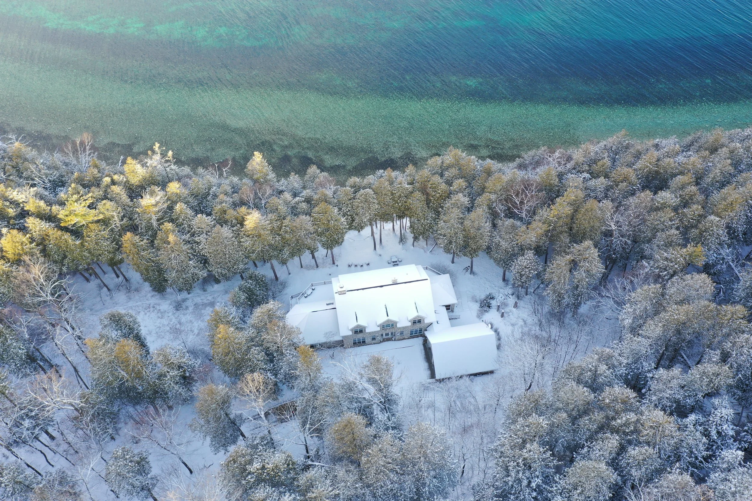 A snow-covered house surrounded by snow-covered trees near a body of water.