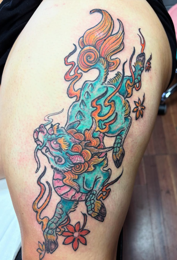 Colorful tattoo of a mythical tiger with flames and flowers on the upper thigh.