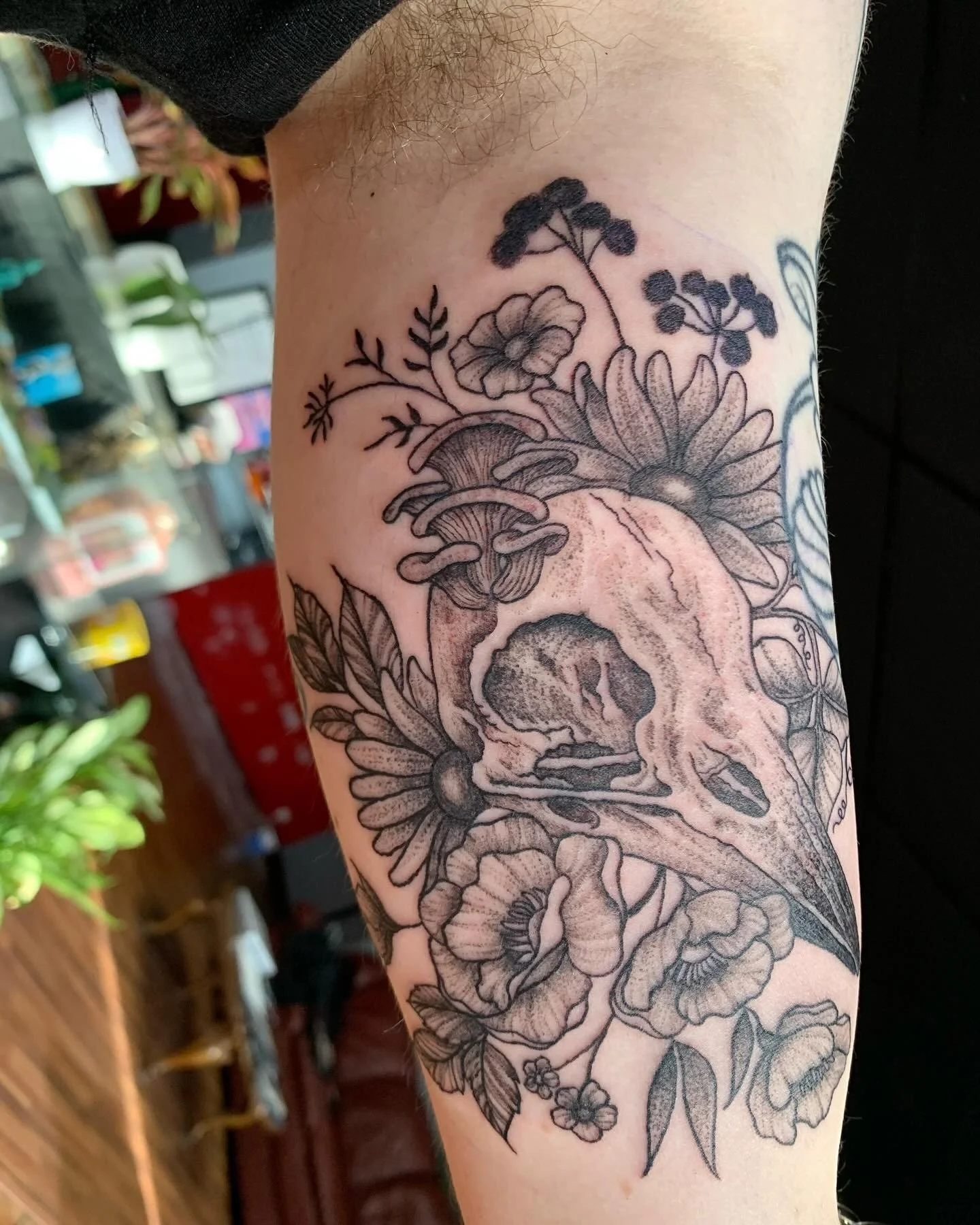 Black and gray floral tattoo on person's arm featuring a skull at the center surrounded by flowers and leaves.
