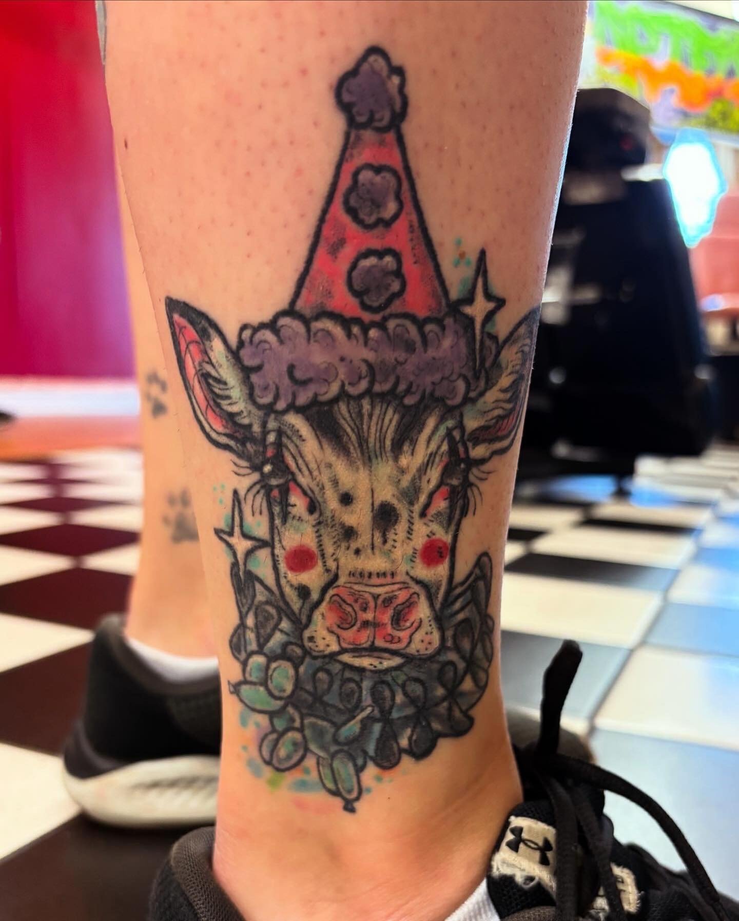 Tattoo of a stylized unicorn with a rainbow-colored mane and a horn, surrounded by stars and clouds, on a person's calf.