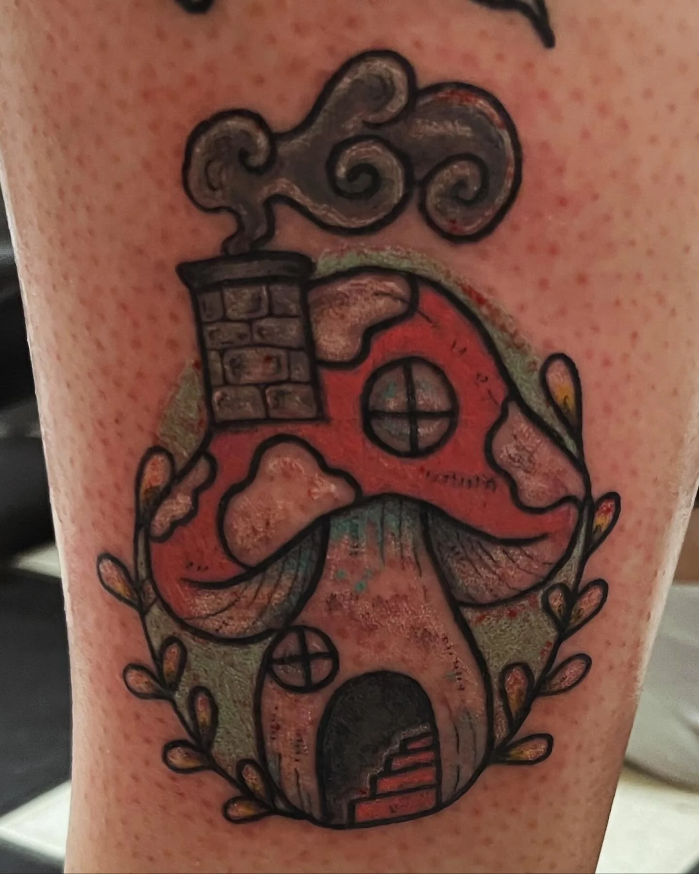 Tattoo of a steaming coffee cup with a spiral swirl of steam, surrounded by leaves, on skin.