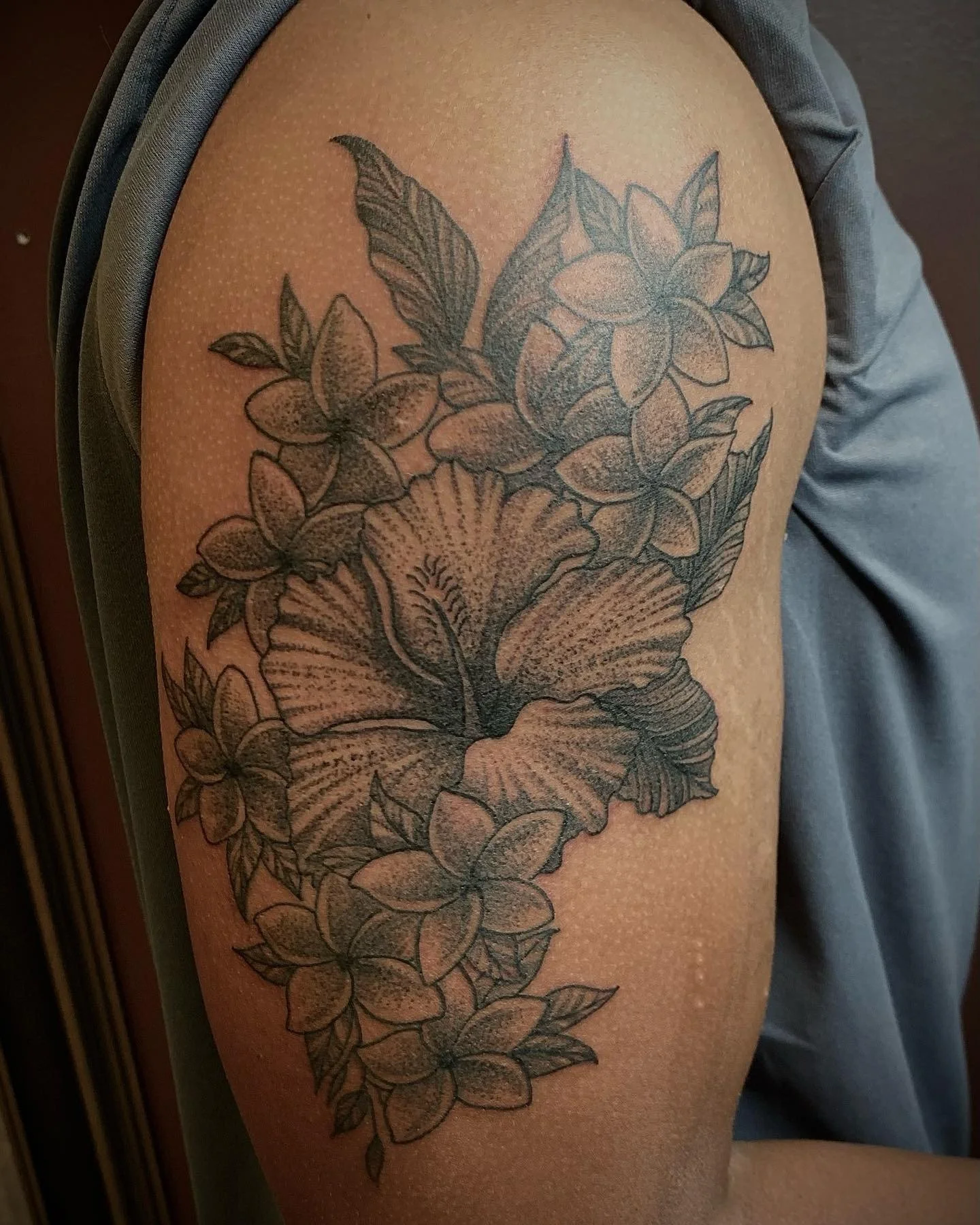 A detailed black and gray floral tattoo on a person's upper arm, featuring large blooming flowers, leaves, and intricate line work.