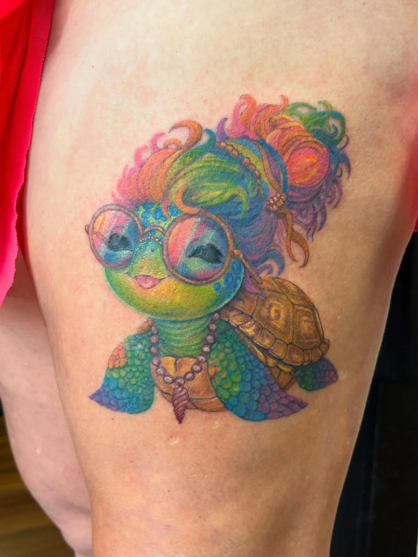 Colorful tattoo of a turtle wearing sunglasses, with a woman with long, curly, rainbow-colored hair.