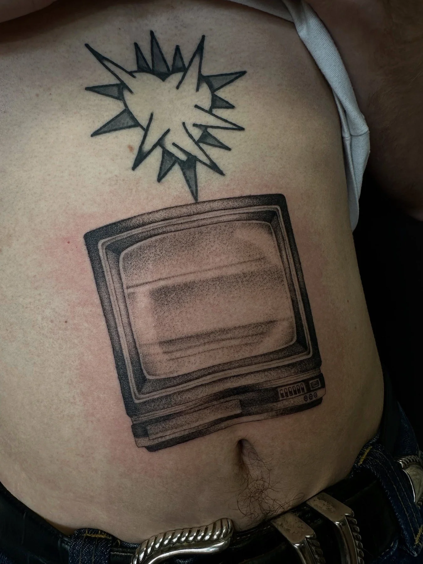 Tattoo of an old-fashioned television on a person's side, and a black and gray explosive starburst design above it.