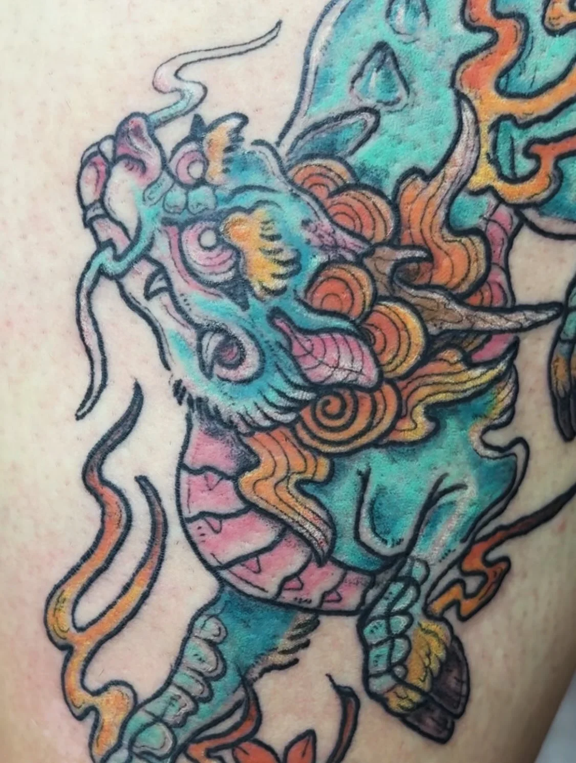Colorful tattoo of a dragon's head with intricate line work and shading.