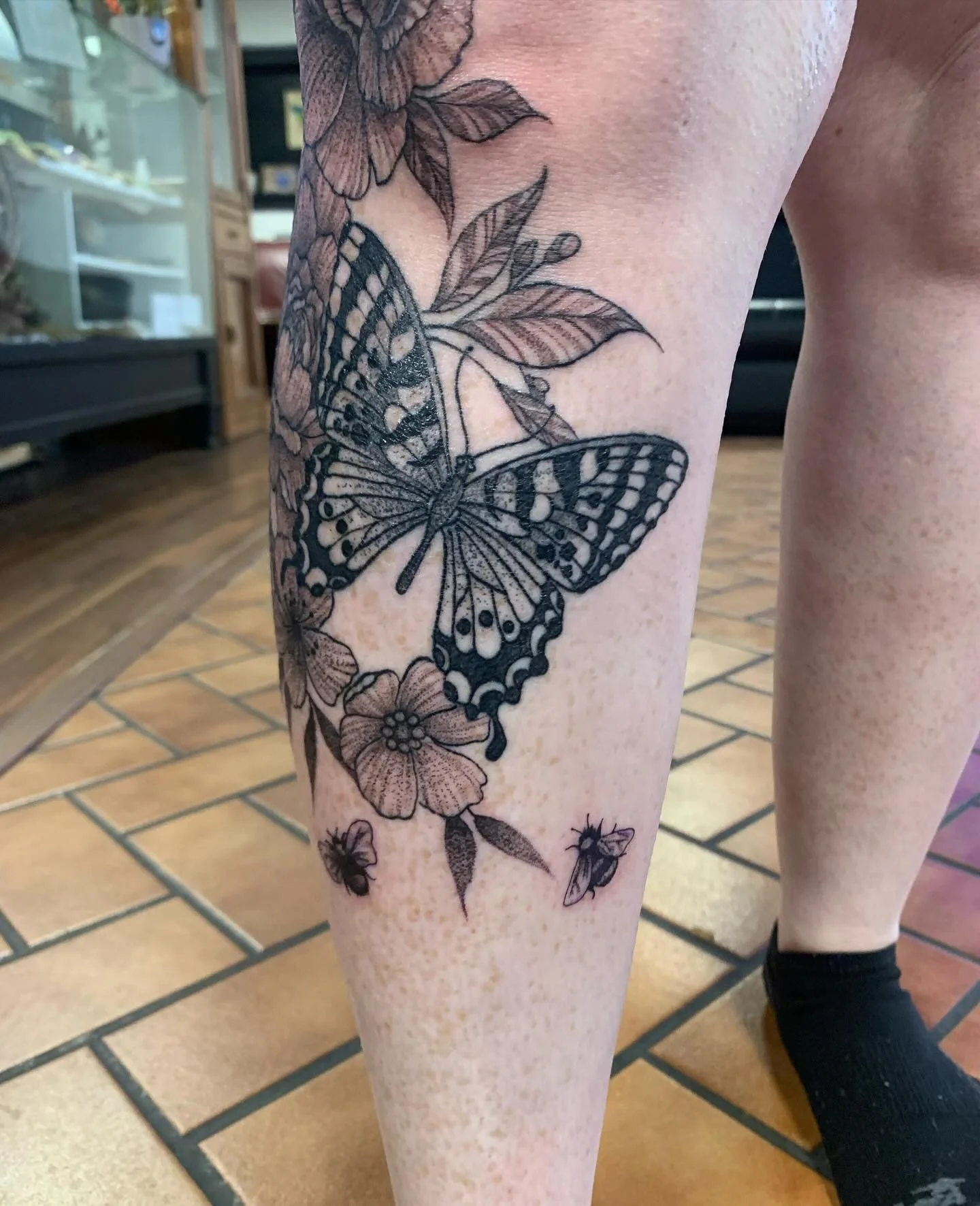 Tattoo of butterflies and flowers on a person's thigh. The tattoo features two large butterflies and several smaller flowers and insects.