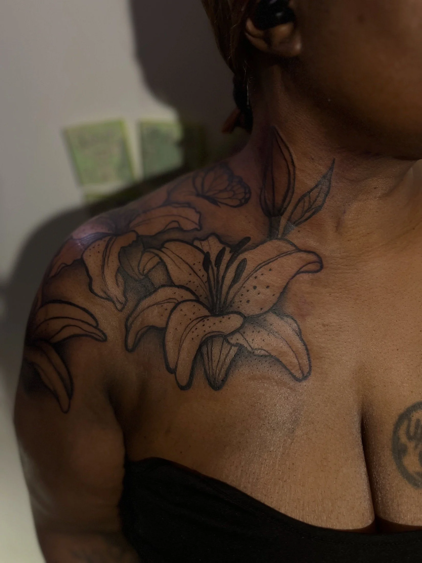 Close-up of a person with a large floral tattoo on their shoulder and chest, wearing a black top.