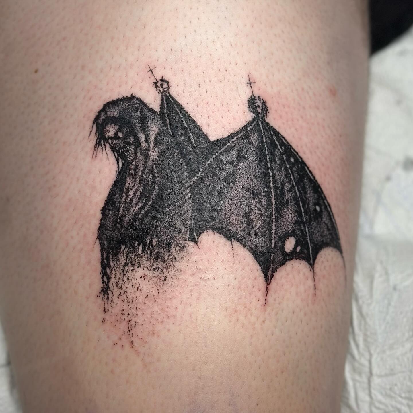 Black tattoo of a bat with detailed wings and face, located on skin.