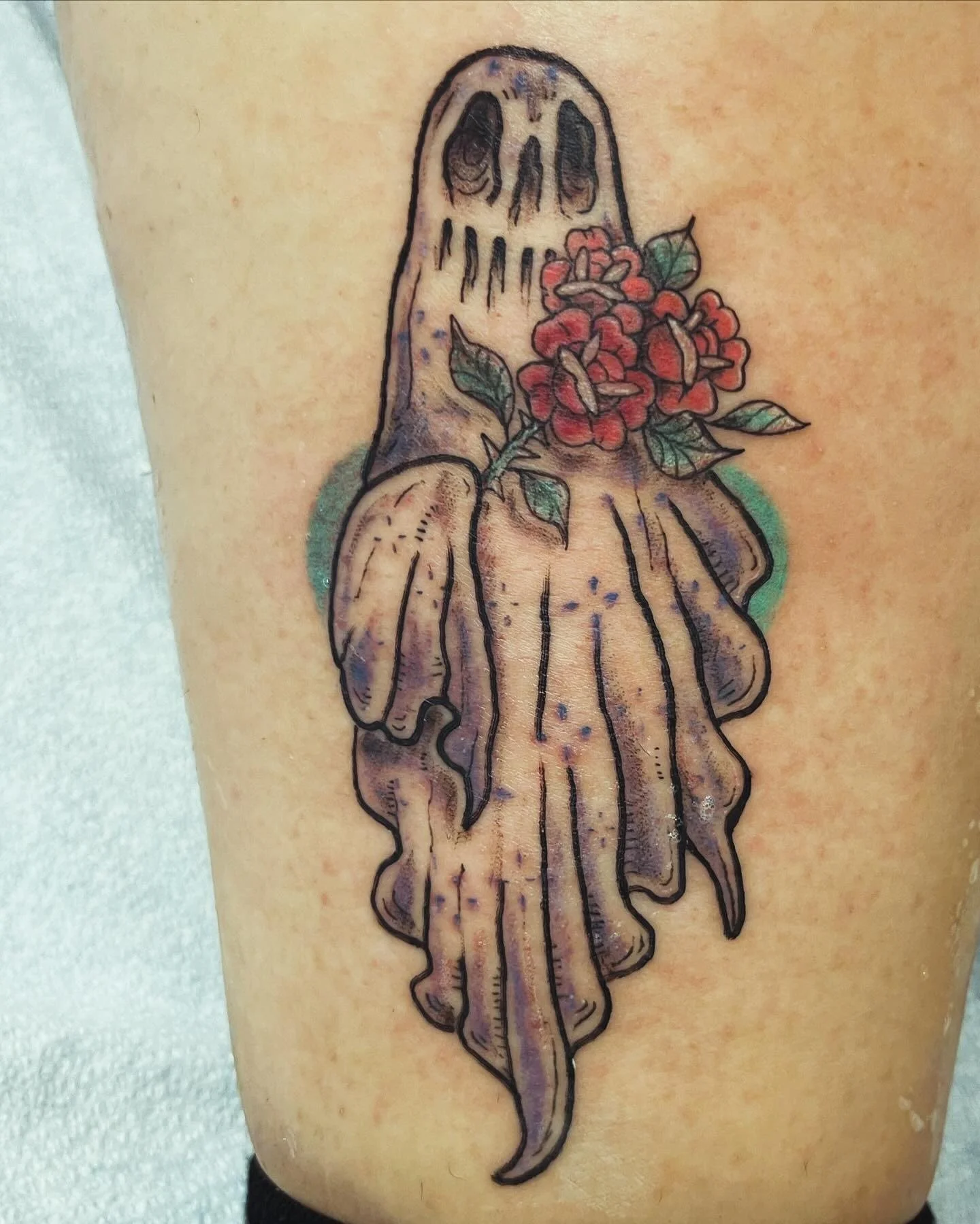 Tattoo of a hand with a bouquet of red flowers and green leaves.