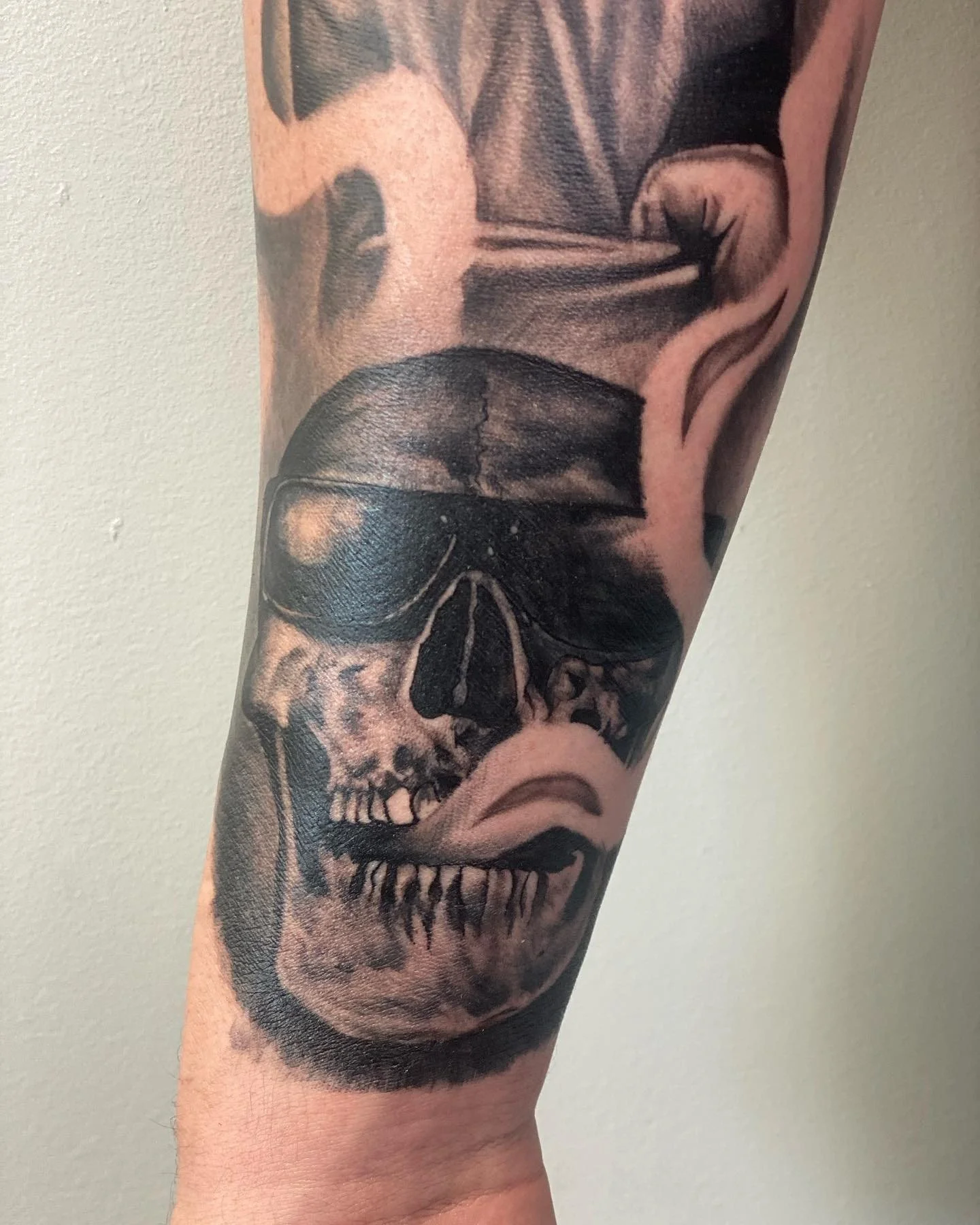Black and grey ink tattoo of a human skull with dark shaded areas on the forehead and cheekbones on a person's arm.