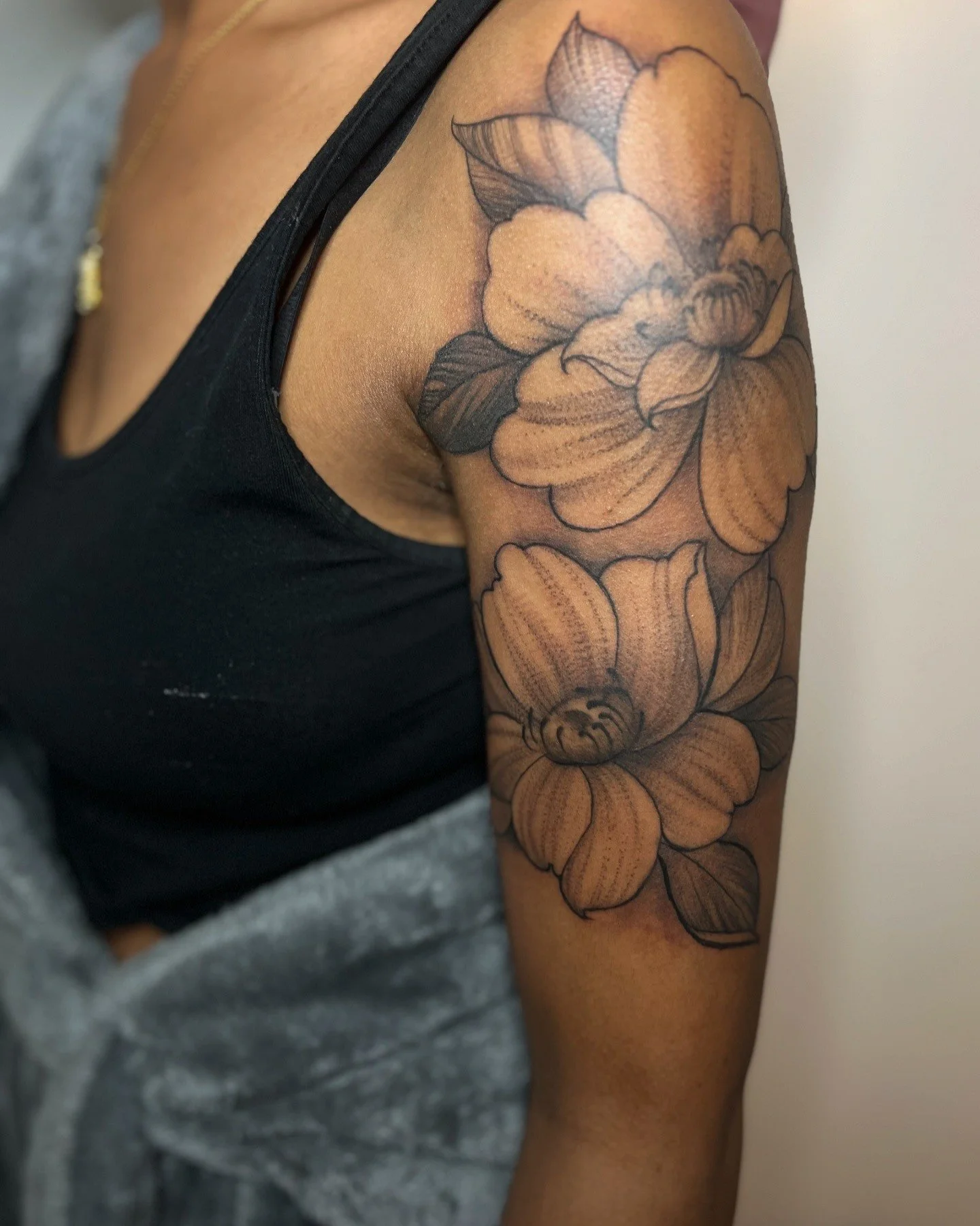 A person with a large floral tattoo on their upper arm, featuring detailed flowers and leaves in black ink.