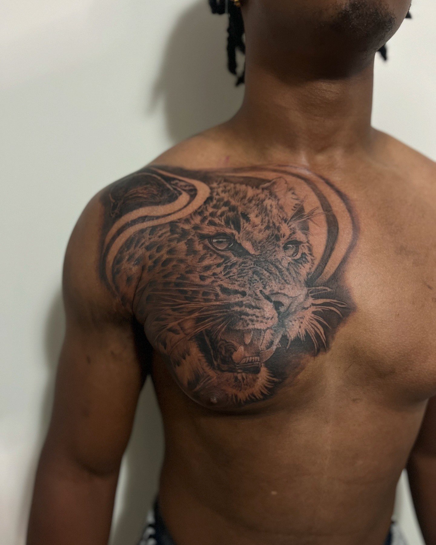 Close-up of a man's upper body, showing a detailed tattoo of a big cat's face on his left shoulder and chest.