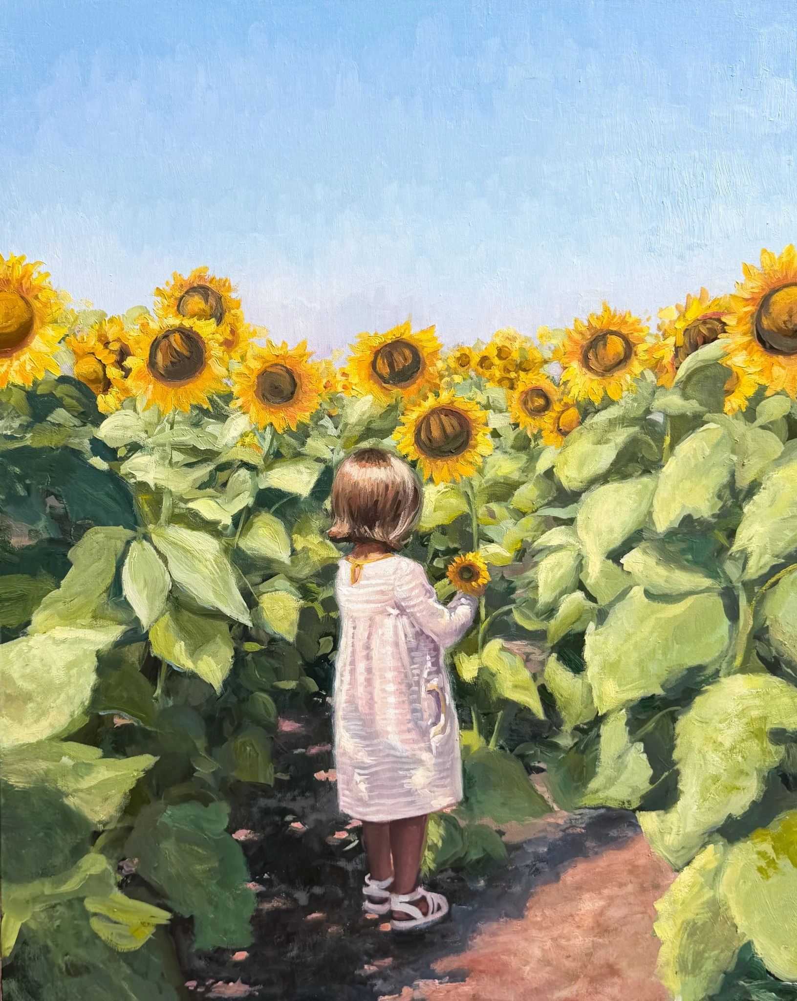 A girl wearing a white dress and sandals walking through a sunflower field, holding a sunflower.