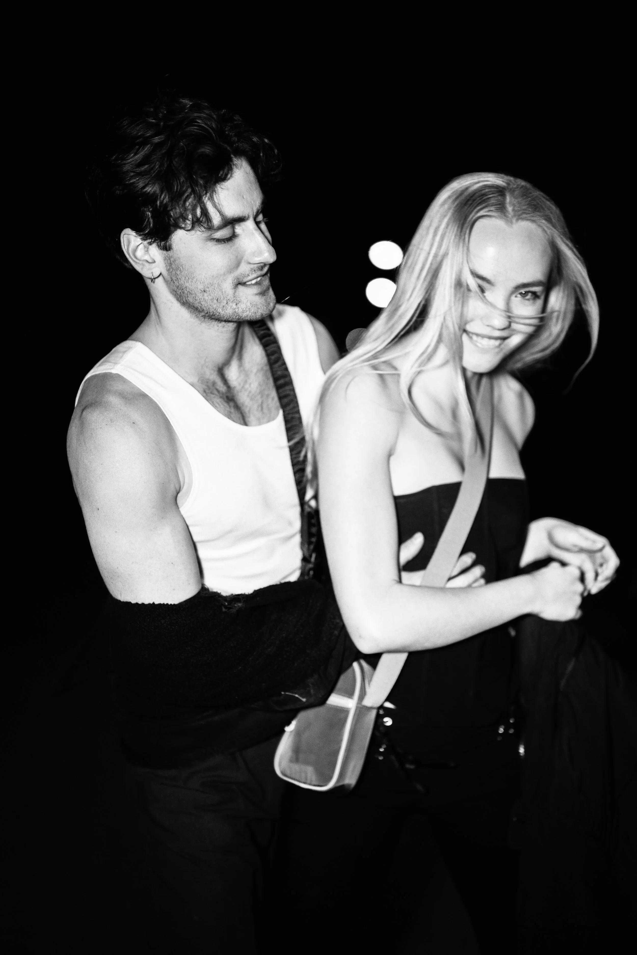 Black and white photo of a young man and woman smiling and enjoying each other's company, standing close together.