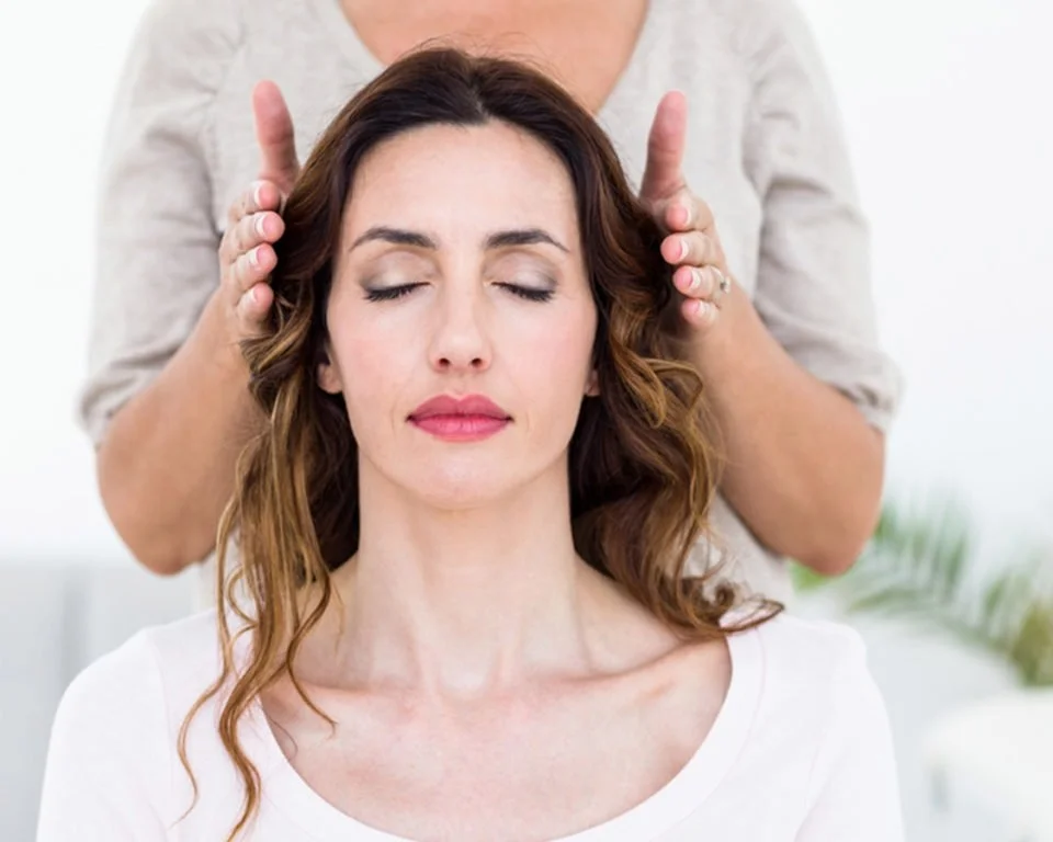 Woman receiving a Reiki session with the practitioner's hands gently positioned on either side of her head.