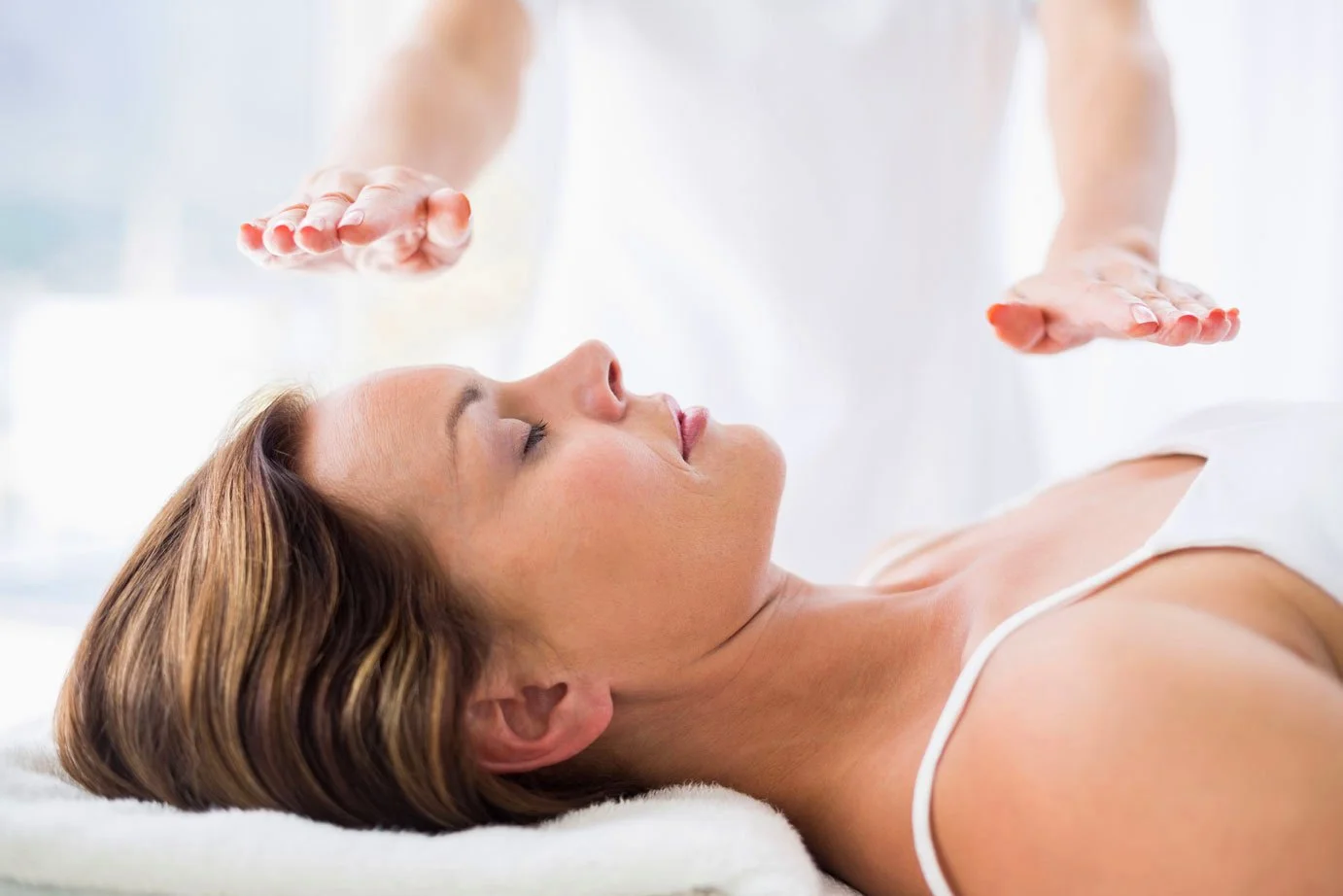 Woman lying on a treatment table while a practitioner holds both hands gently above her body during a chakra balancing session.