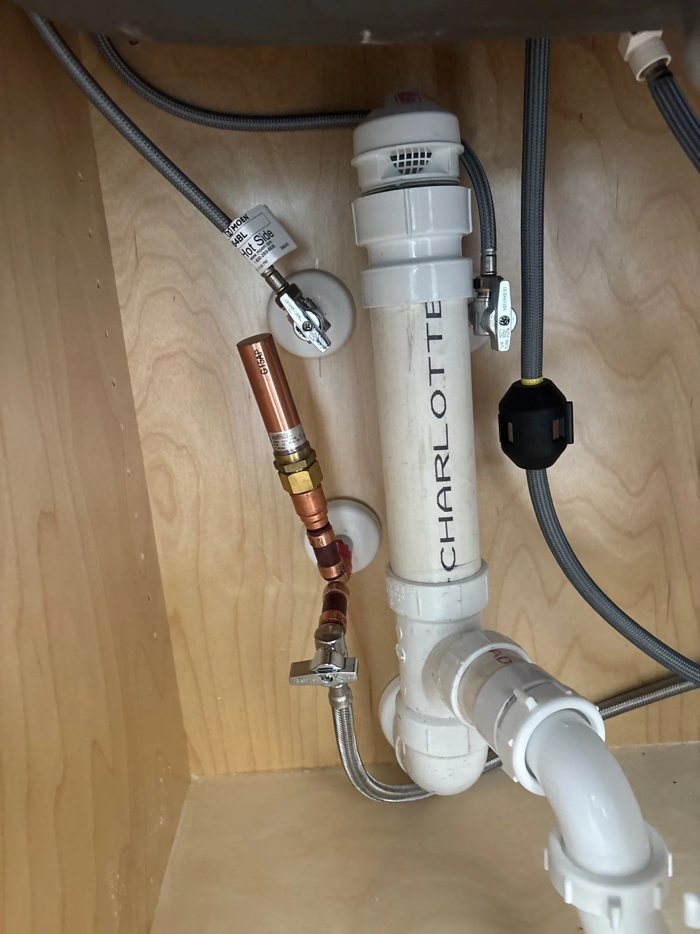 Under sink plumbing with PVC pipes, flexible metal hoses, and copper pipe connected to shut-off valve