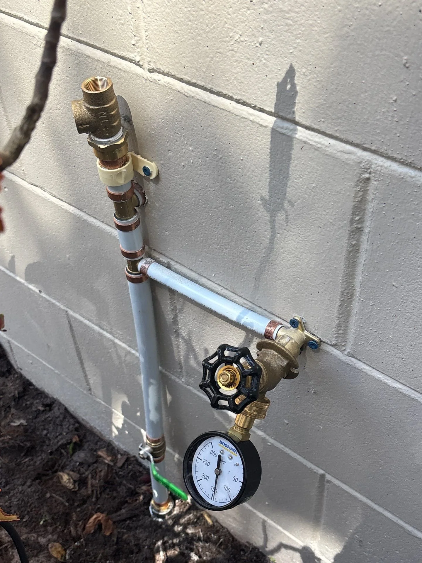 A plumbing setup on a concrete wall featuring a water meter, valves, and pipes with a pressure gauge showing the pressure reading.