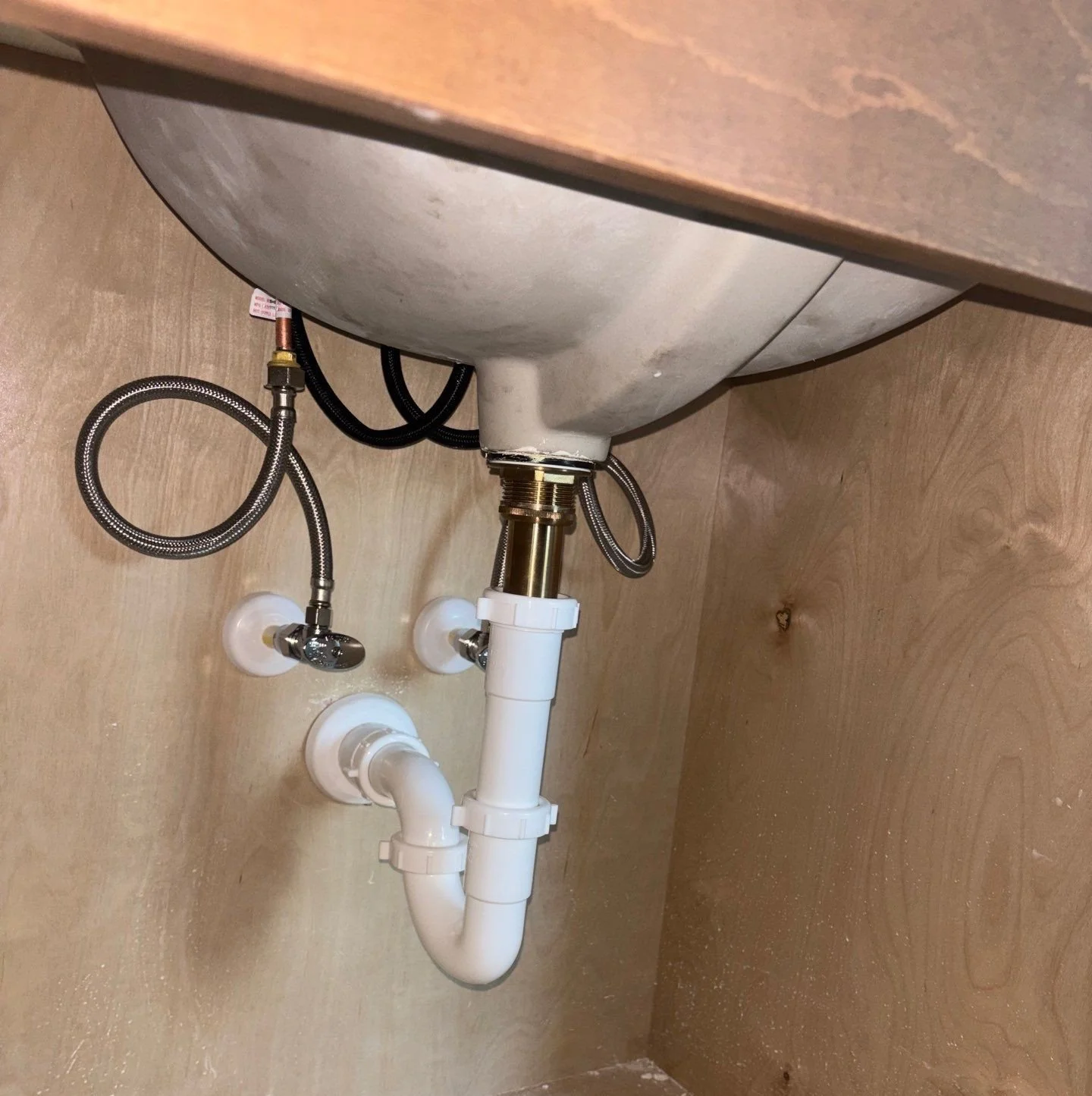 Underneath a kitchen sink showing pipes, hoses, and a shut-off valve.