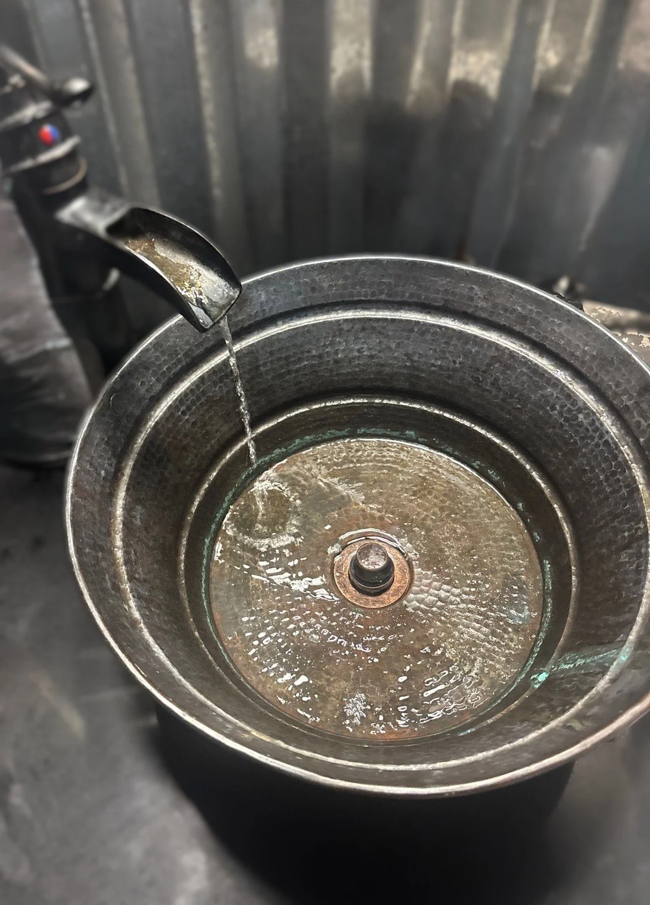 A close-up of a coffee grinder with a small stream of water coming from a faucet into its metal bowl.