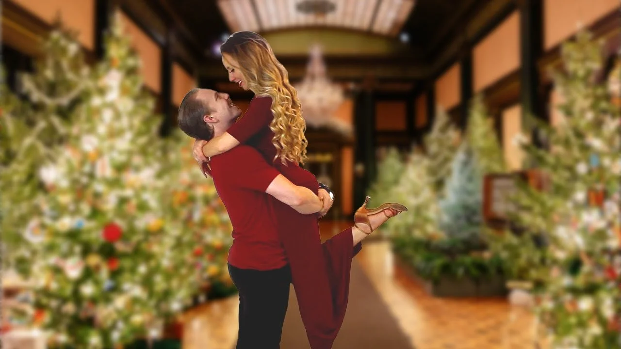 A couple embraces and smiles in a festive hallway, recalling their wedding dances beside Christmas trees and glowing lights.