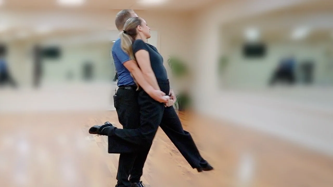 Two people practicing wedding dances in a mirrored studio, holding hands and leaning back as if sharing their first dance.