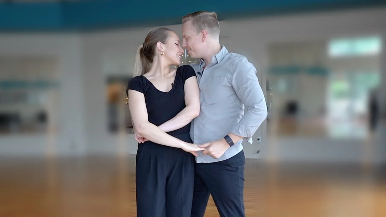 A couple stands close together indoors, smiling and holding hands, sharing a moment like their wedding’s first dance.