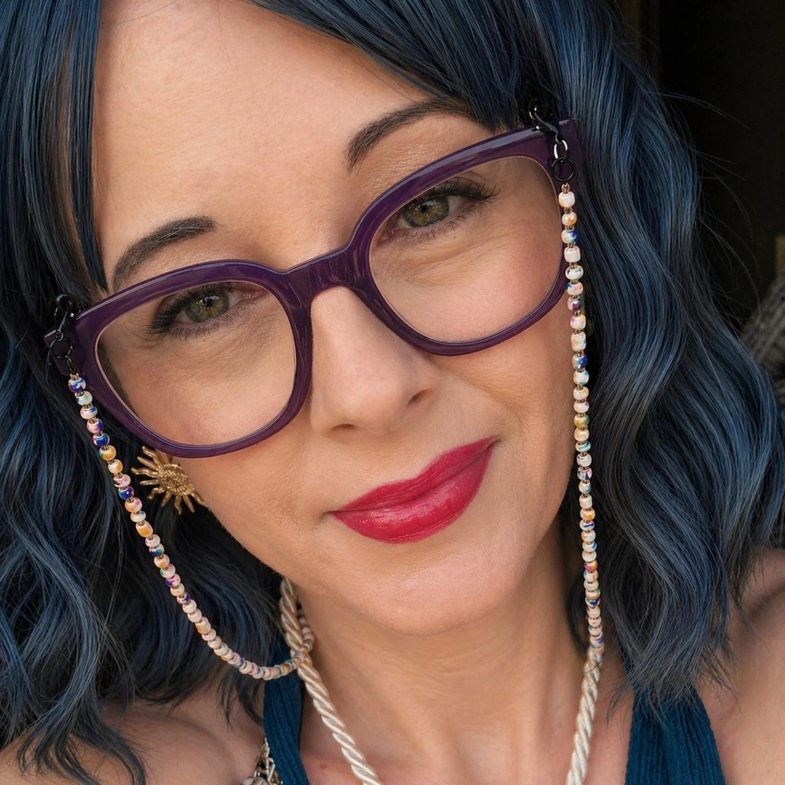 Close-up portrait of Pauline Harley wearing purple glasses and a dark blue wig.