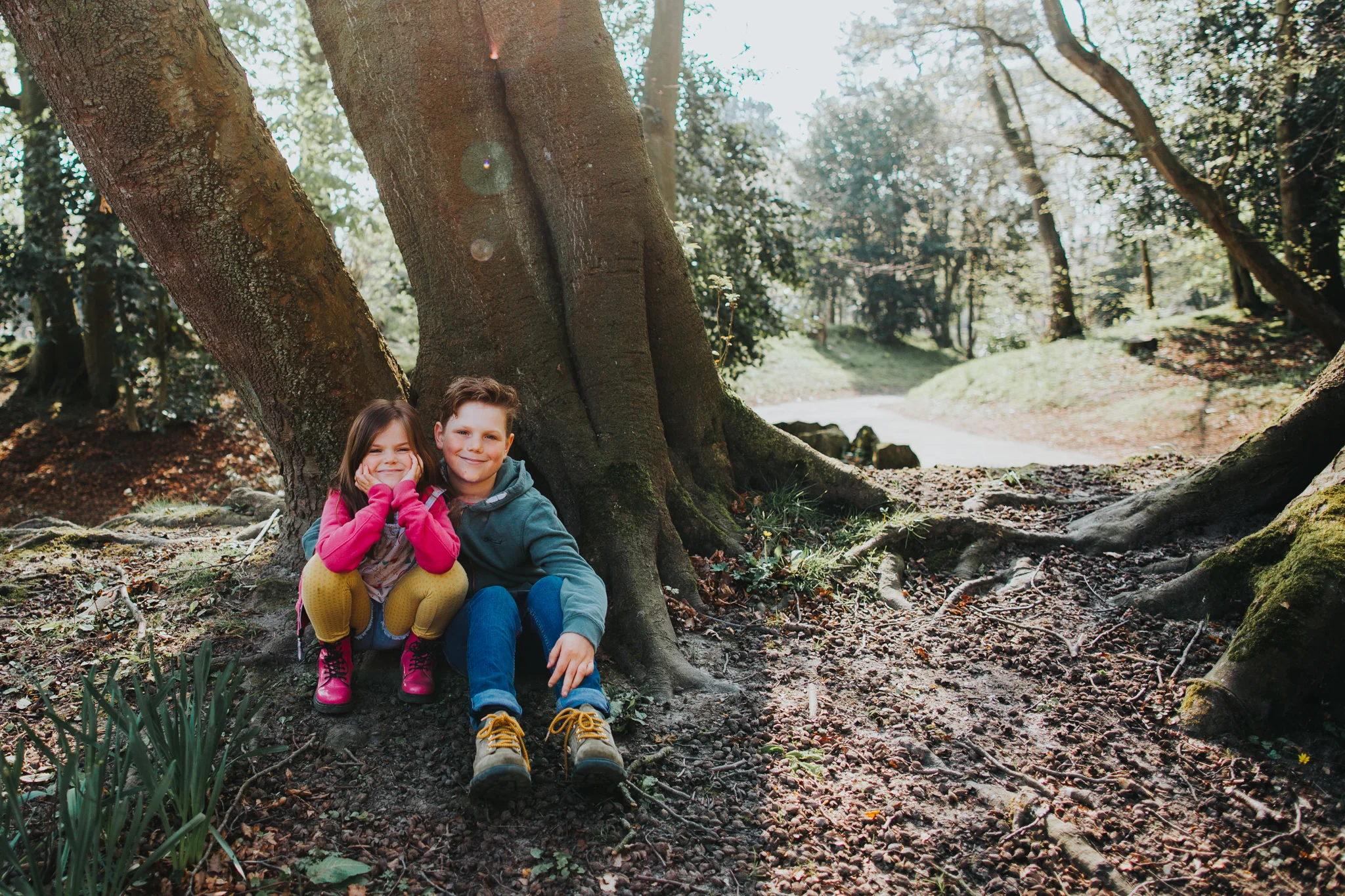 Brother and sister sat down by a tree in the park with sunlight