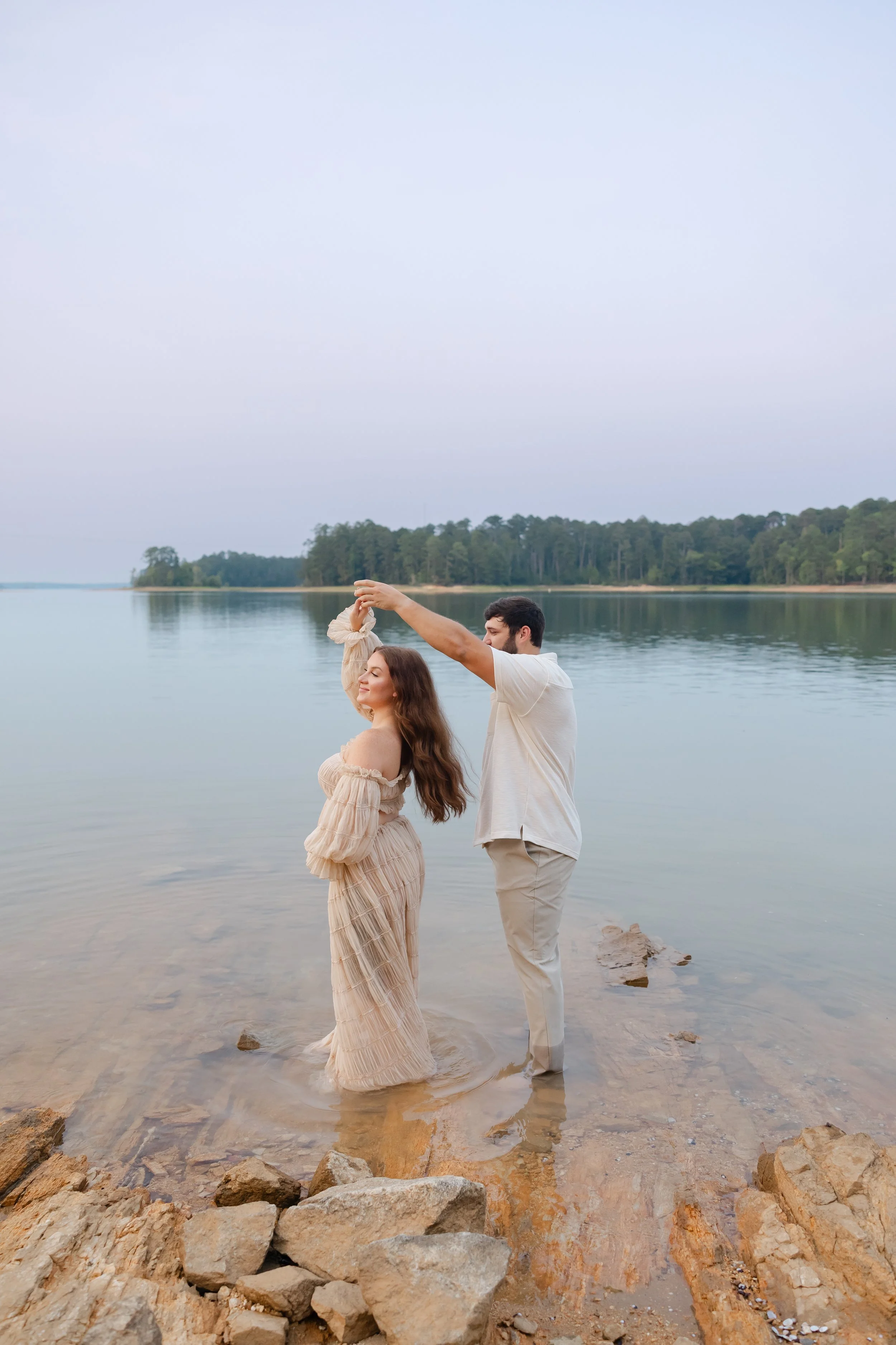 Lakeside maternity session in Appling, Georgia featuring an expecting mother in a flowing cream gown at sunset by the water.