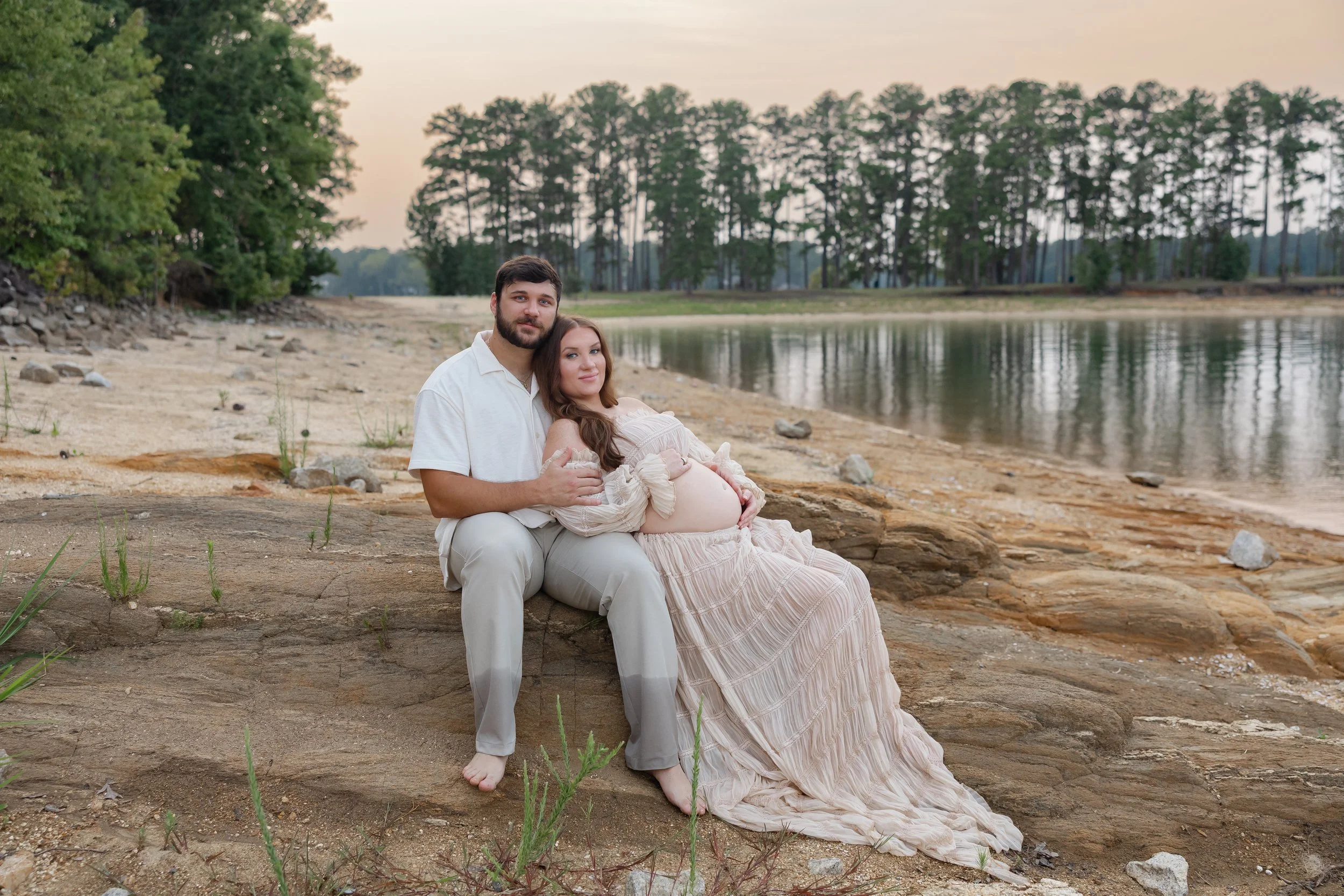 Couple celebrating pregnancy during a lakeside maternity session in Appling, Georgia with golden sunset light.