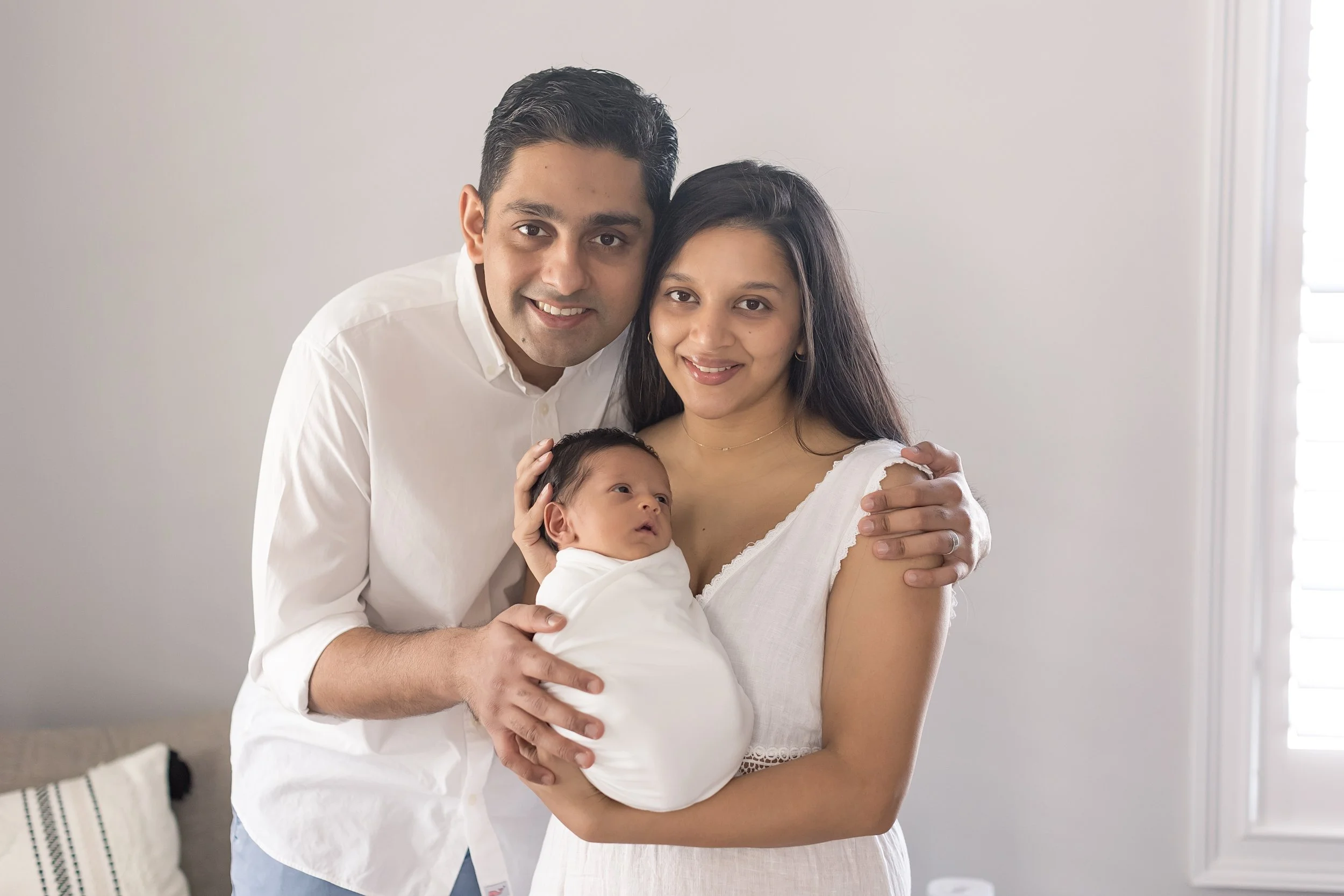 family smiling at camera holding their newborn baby boy at their inhome newborn photography session in Evans, ga
