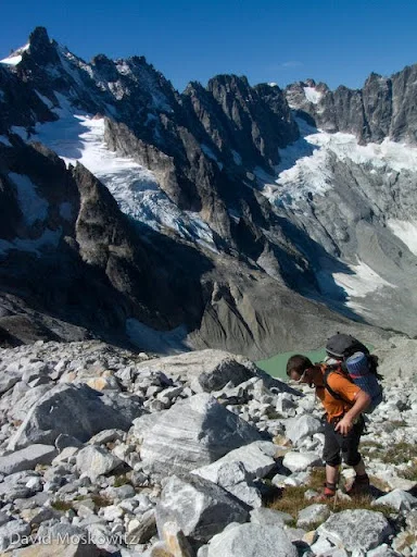 Forest McBrian hiking out of Luna Cirque with the massive north face of Mount Fury rising on the left and Luna lake below.