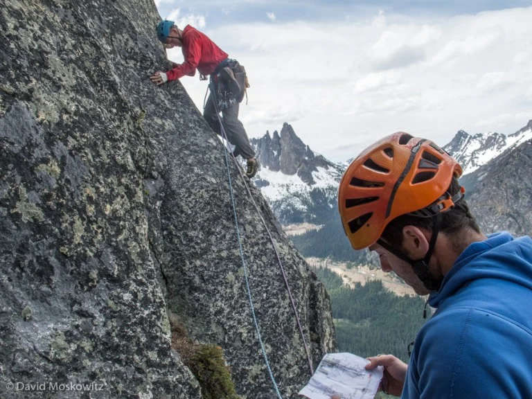 Josh Cole reviews the route description as Ryan sets off on another pitch of the route. Liberty Bell and the road cut of the North Cascades Scenic Highway can be seen in the distance.