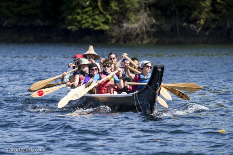 Members of the Blue Heron Canoe family and students of the LEAF school paddle the canoe along the shores of an island on the central coast of British Columbia.