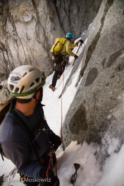 We crossed the burgshrund on the top of the glacier at first light and ascended the lower section of the couloir, about 40-50 firm snow, which runs up the northwest face of the peak. At the narrowest section of the couloir are two steps of steeper terrain. Here Joel Reid leads out to climb a pitch of mixed rock, ice, and snow with a belay from Trever Waage. Trevor lead the next step of ice.