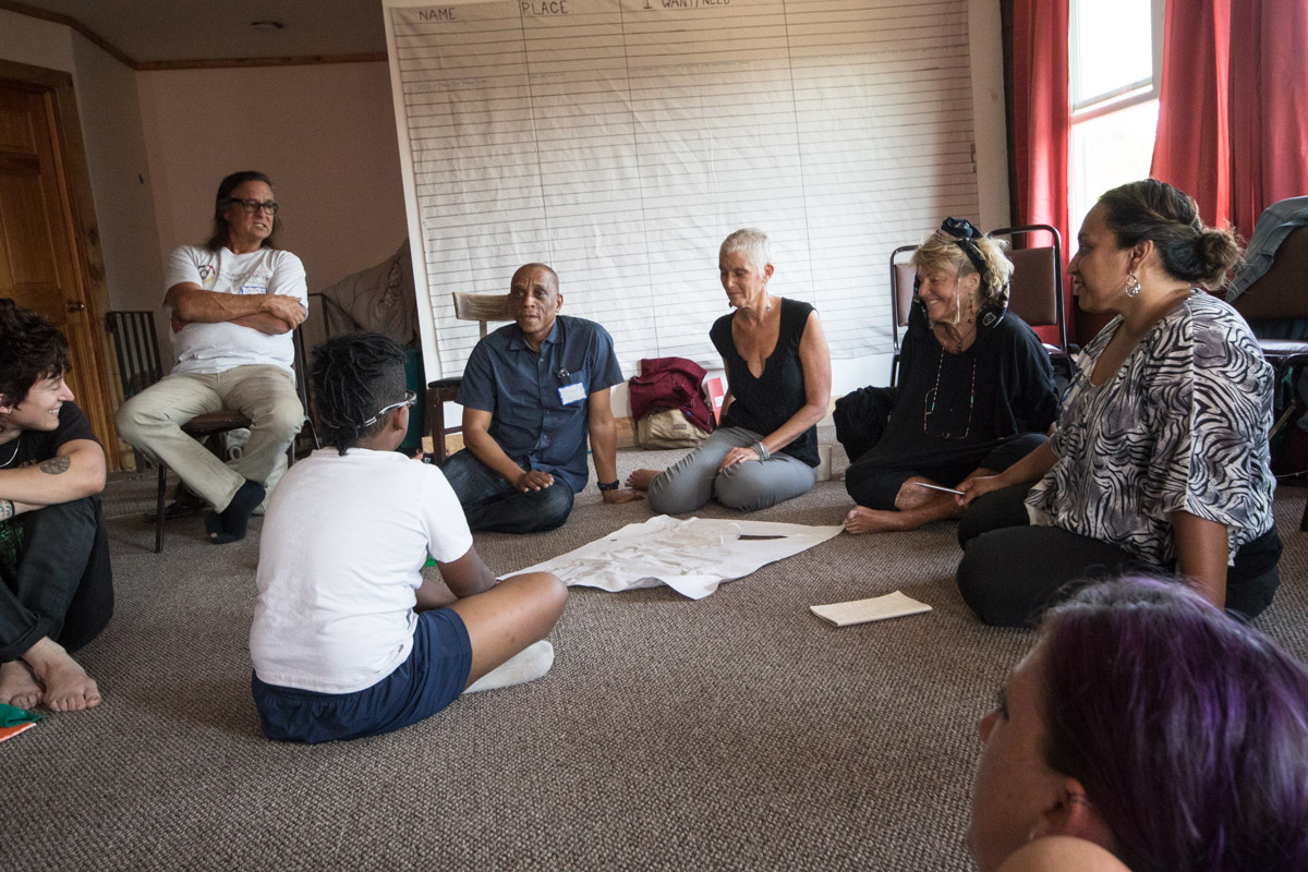 A young member of the gathering sits with a group of olders and elders to ask them to explain a piece of art they created.