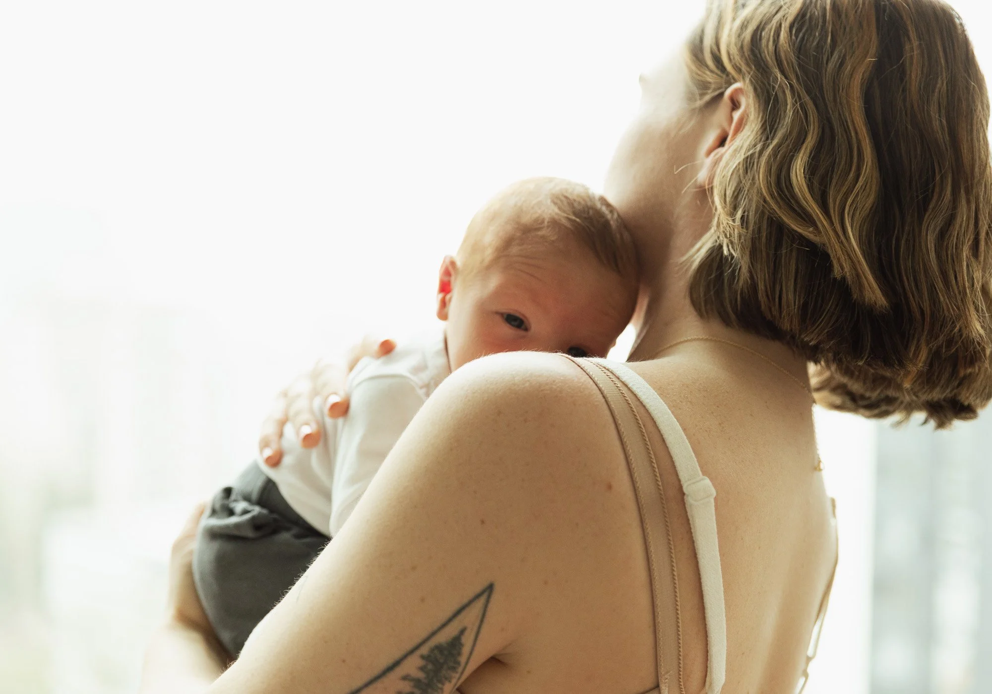 A woman holding a young child close to her shoulder indoors, with soft natural light in the background.