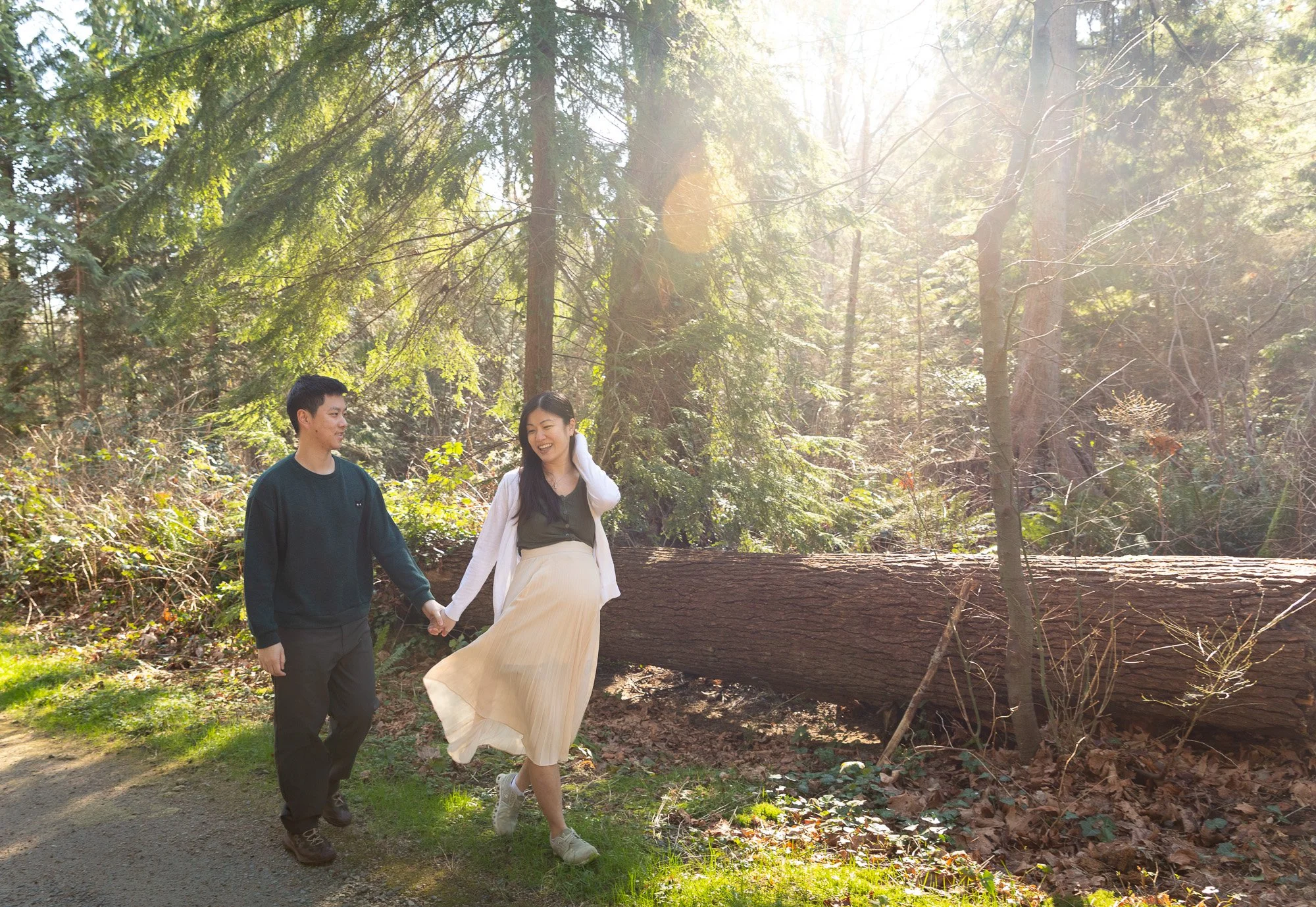 A couple walking hand in hand in a forest with sunlight filtering through the trees.
